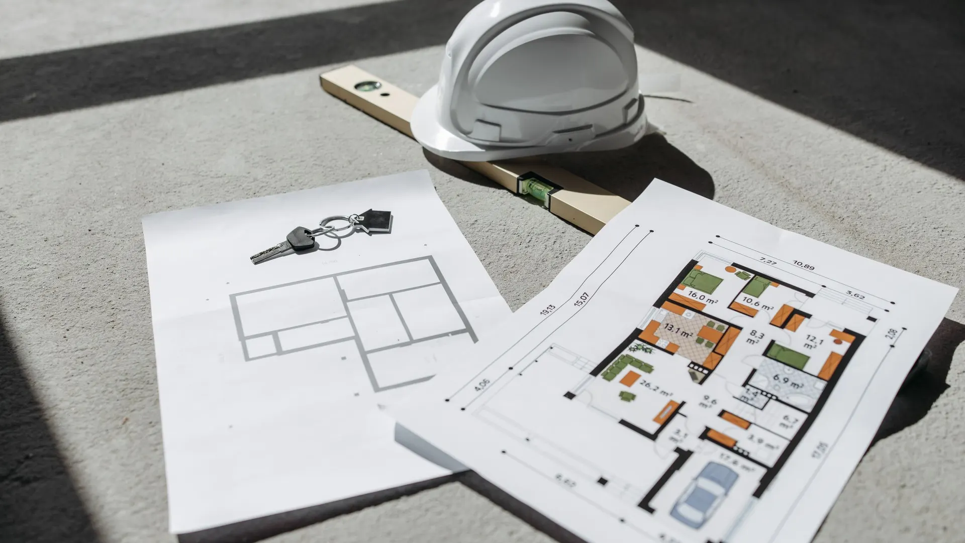 Architectural floor plans on a table with a hard hat and keys